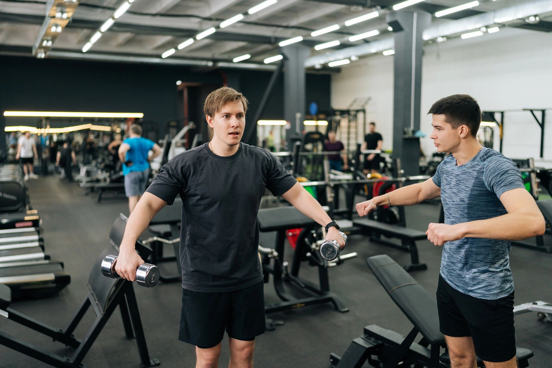 Personal trainer assisting a client with dumbbell training in the gym
